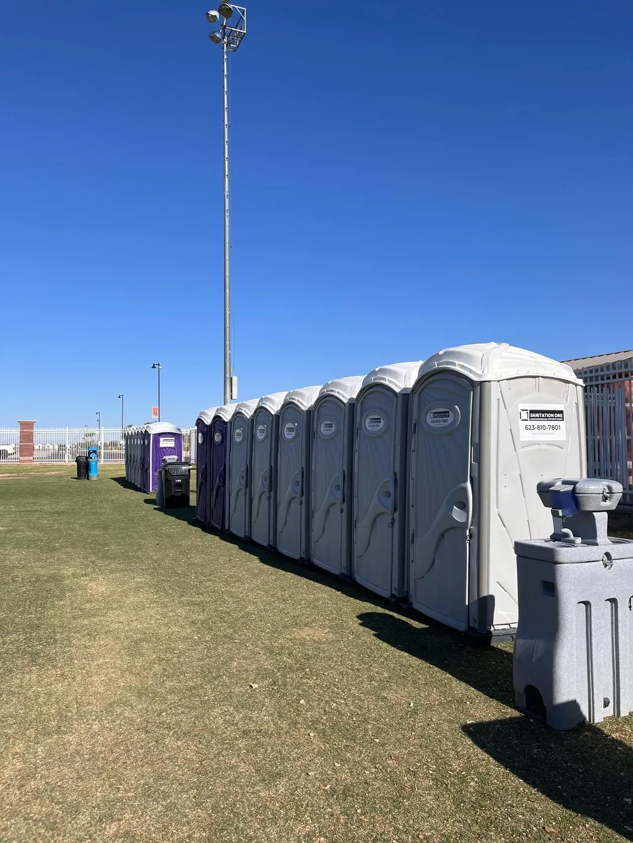 Row of Sanitation One portable toilets and a hand wash station at an outdoor sports field